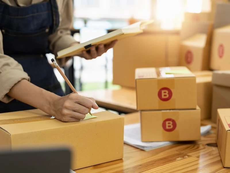 young asian woman writing address on parcel box